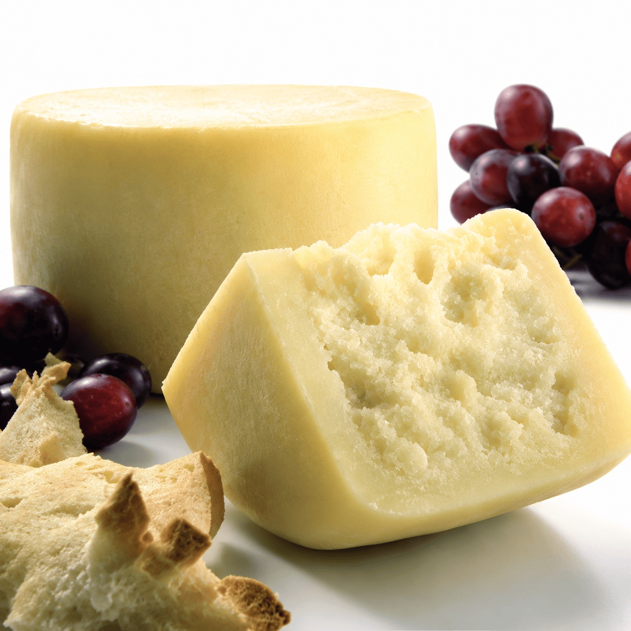 A wheel of Pecorino Lupa beside a cut wedge, with grapes and carasau bread